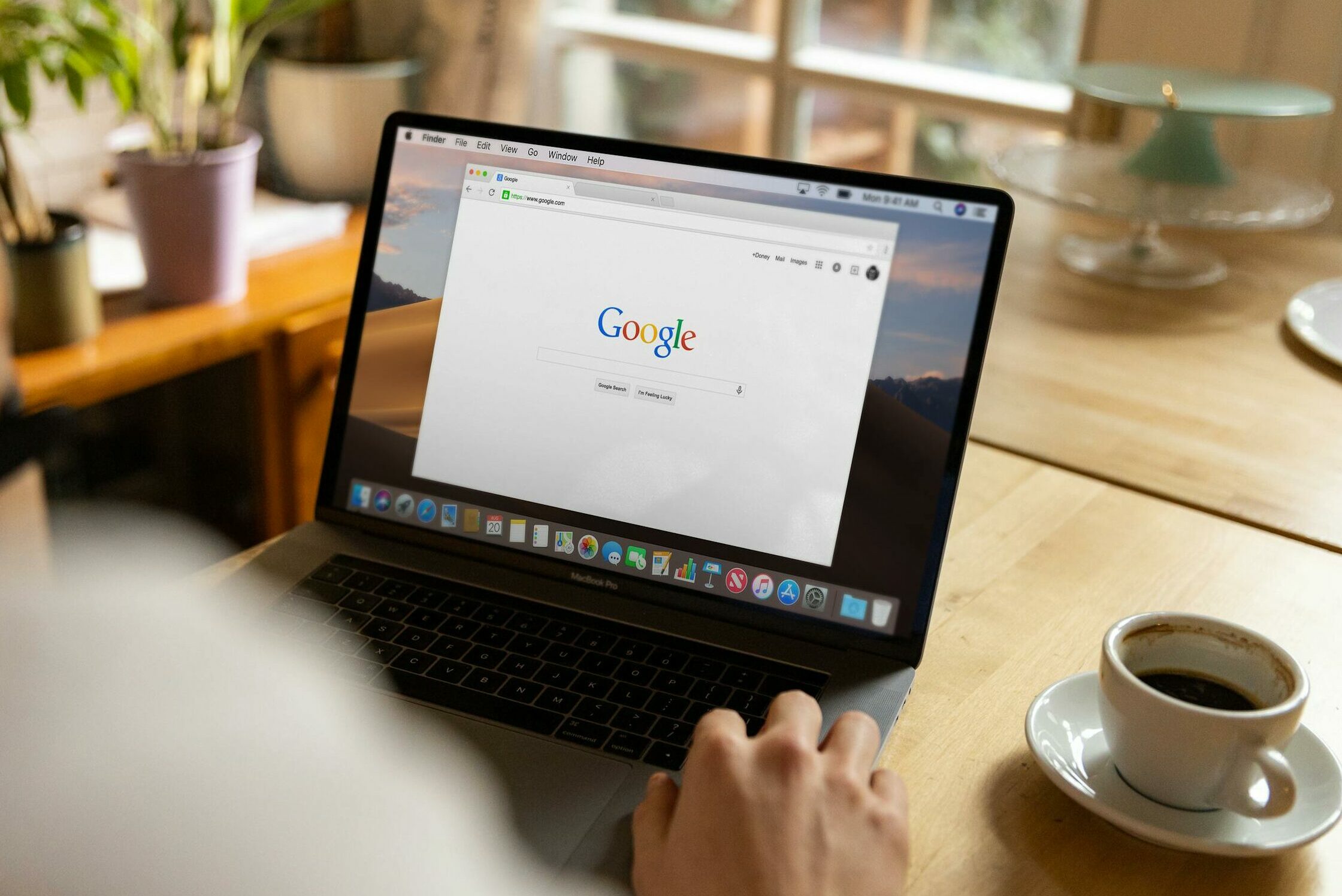 An adult using a laptop indoors, browsing Google at a wooden table with coffee.